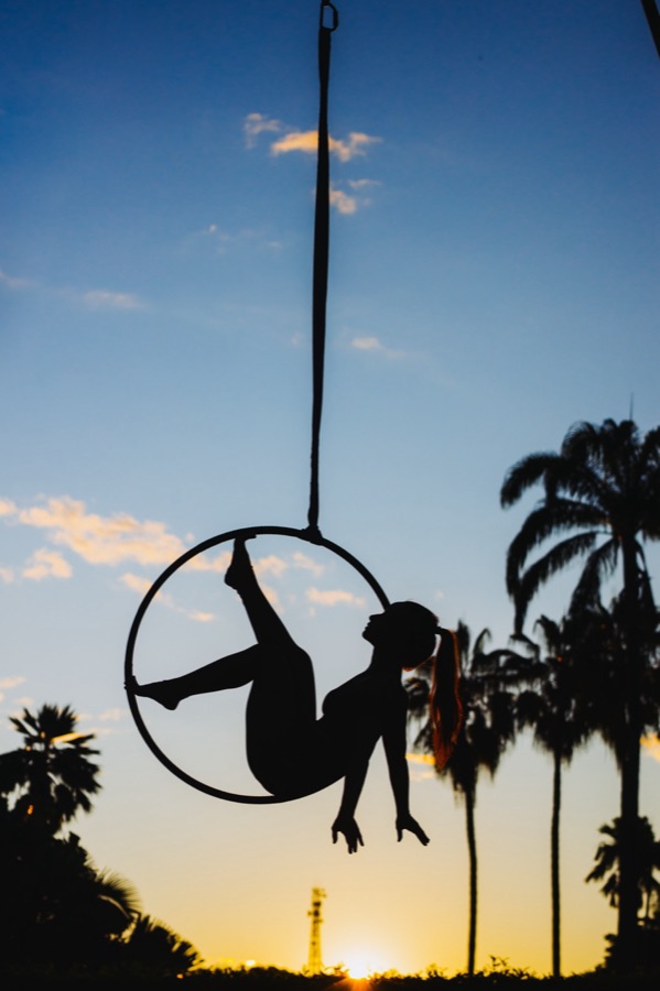 An aerial hoop performer silhouetted against a sunset